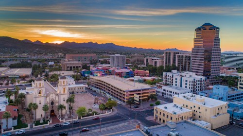 Aerial view of a cityscape at sunset, featuring buildings, mountains, and a historic church in the foreground.