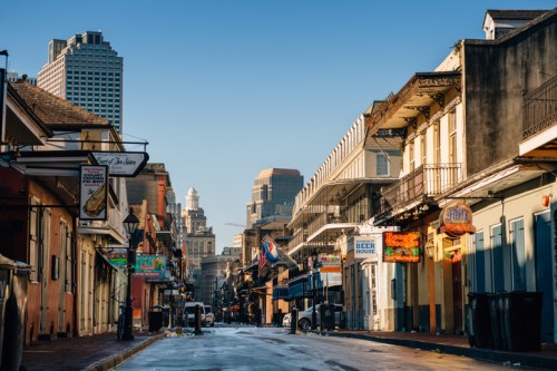 Empty street in New Orleans with historic buildings, colorful signs, and a clear blue sky in the background.