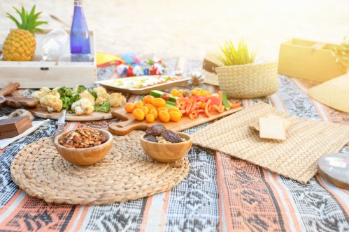 A vibrant picnic spread with fruits, vegetables, snacks, and drinks on a patterned blanket under warm sunlight.