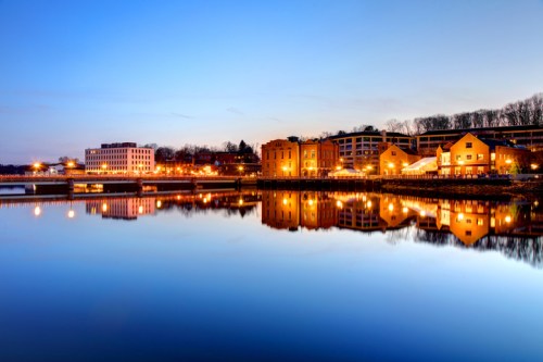 A serene evening scene of a river reflecting buildings and lights, with a clear blue sky above.