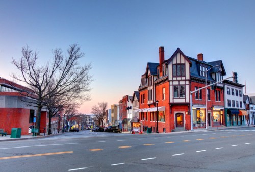 A street view of a charming town with historic buildings, trees, and a clear sky at dusk.