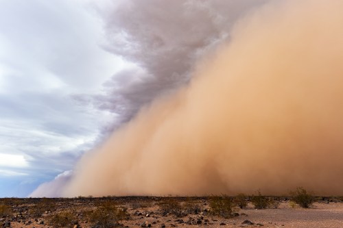 A vast dust storm rolls across a barren landscape, with dark clouds above and a swirling cloud of dust below.