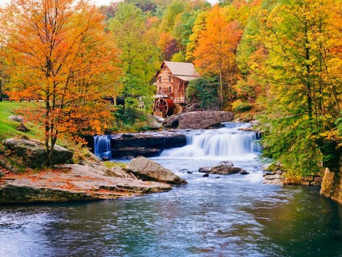 A scenic view of a wooden mill by a waterfall, surrounded by vibrant autumn foliage and a calm river.