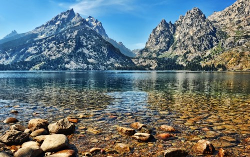 A serene lake surrounded by majestic mountains, with clear water revealing smooth stones beneath the surface.