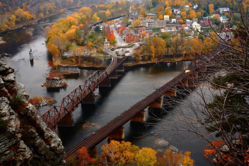 Aerial view of a river winding through a colorful autumn landscape with a town and railway bridge in the foreground.