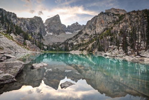 A serene mountain lake reflects towering peaks and lush greenery under a colorful sky.