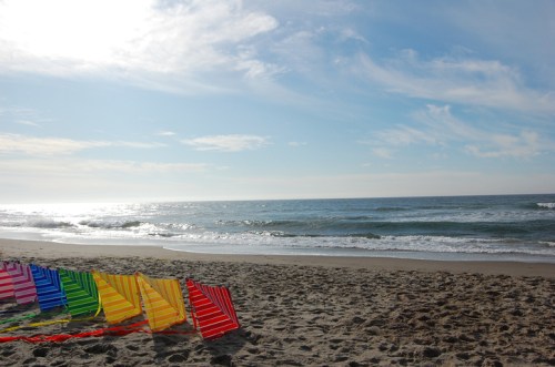 Colorful beach chairs lined up on sandy shore with gentle waves and a clear blue sky in the background.