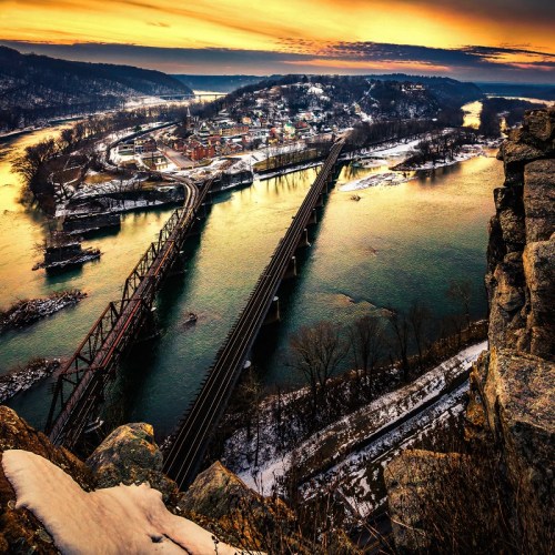 A scenic view of a river and bridges at sunset, with snow-covered banks and a small town in the background.