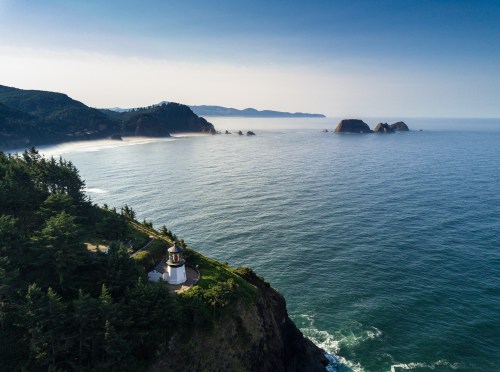 A scenic coastal view featuring a lighthouse on a cliff, with rocky islands and calm ocean waters in the background.