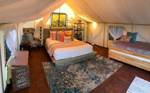 Cozy glamping tent interior with a queen bed, twin bed, decorative pillows, and a rug. Warm, inviting atmosphere.