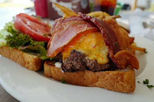 A juicy burger topped with melted cheese, crispy bacon, lettuce, and tomato, served on toasted bread with fries.