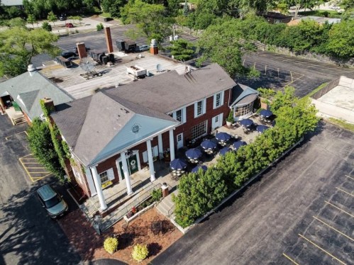 Aerial view of a restaurant with outdoor seating, surrounded by trees and a large parking lot.