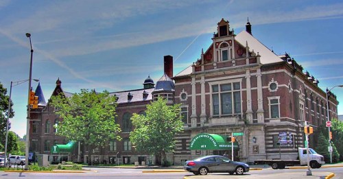 Historic brick building with ornate architecture, surrounded by trees and a clear blue sky.