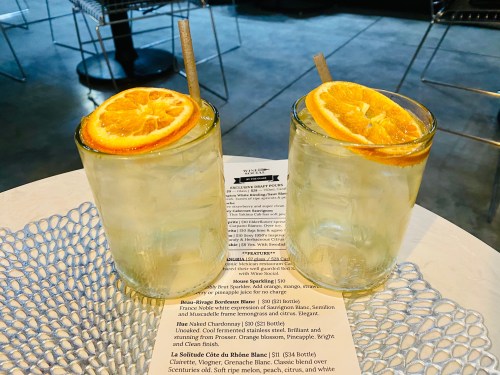 Two cocktails with orange slices on a table, accompanied by a menu in a stylish setting.