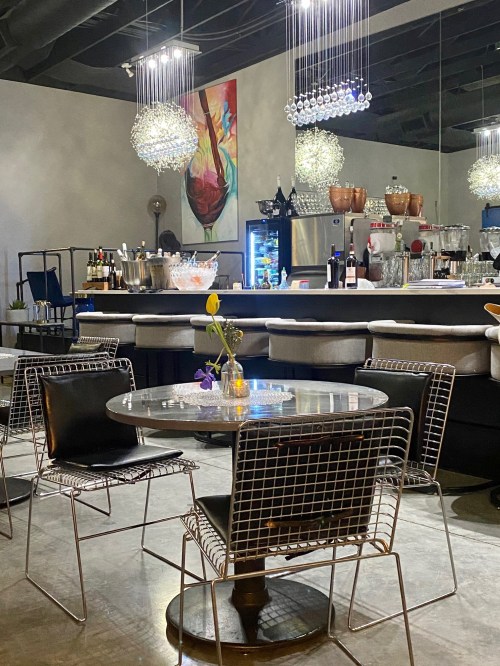 A modern restaurant interior featuring a round table, wire chairs, and stylish pendant lights above a bar area.