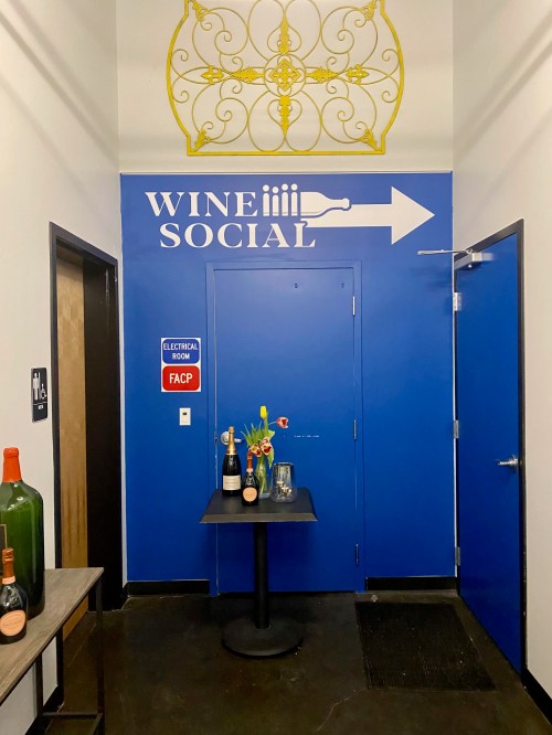 A blue wall with "WINE SOCIAL" sign and an arrow, featuring a table with champagne and flowers nearby.