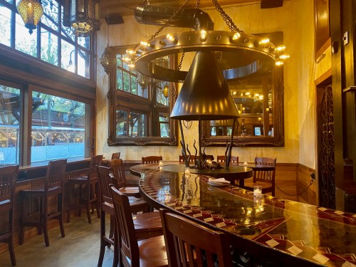 Cozy restaurant interior featuring a large chandelier, wooden bar, and ornate mirrors with warm lighting.