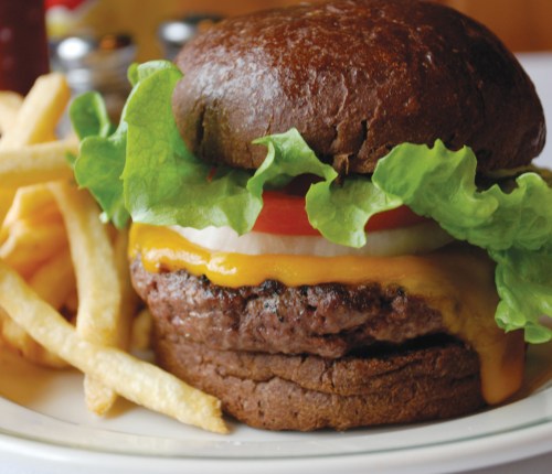 A juicy burger with lettuce, tomato, and cheddar cheese on a dark bun, served with a side of golden fries.
