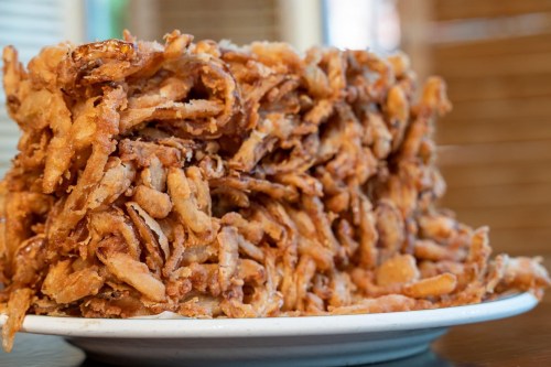A large pile of crispy, golden-brown fried onions on a white plate.
