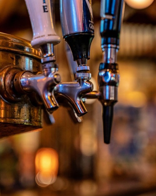 Close-up of beer taps with shiny metal handles, set against a blurred bar background.