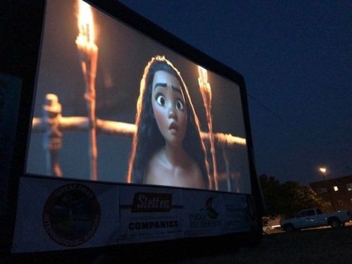 A large outdoor screen displays an animated character with long hair, looking surprised in a nighttime setting.