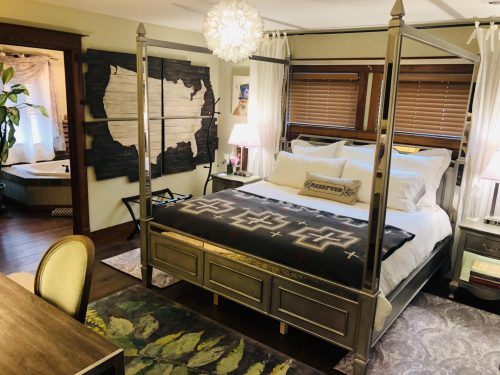 A cozy bedroom featuring a four-poster bed, decorative pillows, a desk, and warm lighting.