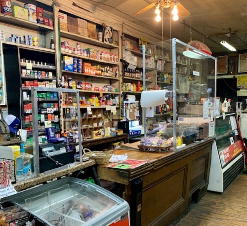 A vintage store interior with shelves of products, a checkout counter, and a protective glass barrier.