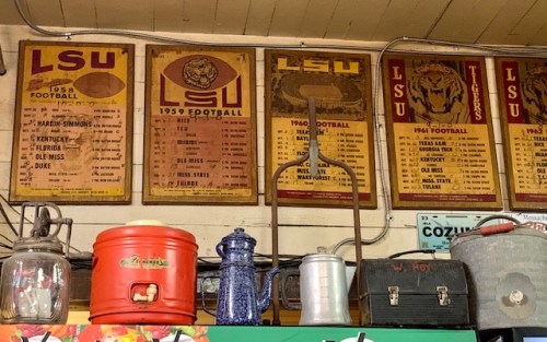 Vintage LSU football posters from 1958 to 1964 displayed on a wall, with various antique items in the foreground.