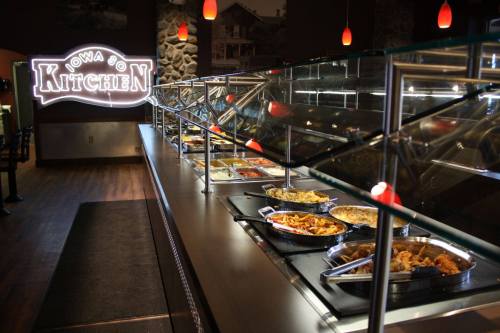 A buffet line featuring various dishes under glass, with a sign reading "Iowa Kitchen" in the background.
