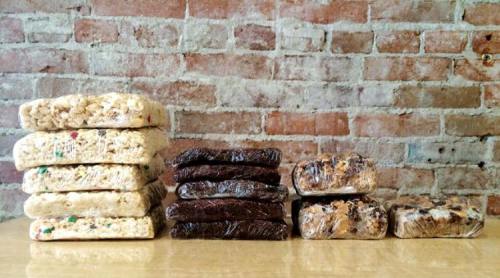 A variety of stacked rice crispy treats in different flavors against a rustic brick wall.