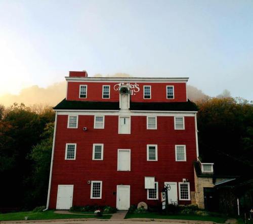 A large red building with white trim, surrounded by trees and a misty mountain backdrop.