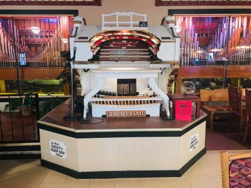 A vintage organ on a pedestal in a venue, with a microphone and decorative elements in the background.
