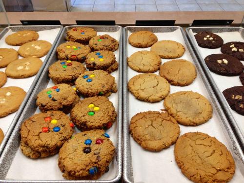 A variety of freshly baked cookies on trays, including chocolate chip, peanut butter, and colorful candy cookies.