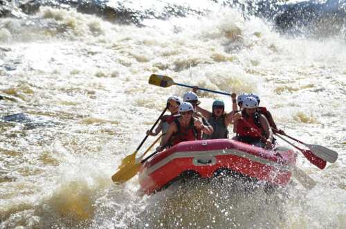 A group of four people in a red raft navigating through turbulent whitewater rapids.