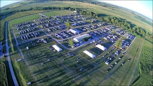 Aerial view of a large campground with numerous tents and RVs set up in a green, open landscape.