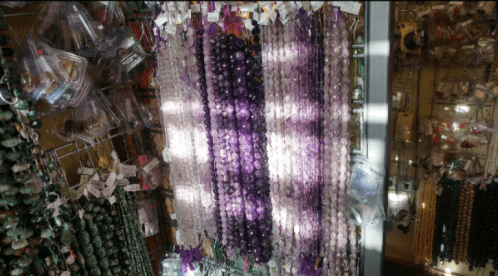 Colorful strands of beads in various shades, hanging in a display with other decorative items in the background.