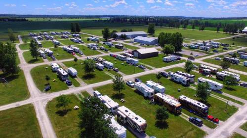Aerial view of a spacious RV park with numerous parked RVs and green fields in the background under a blue sky.