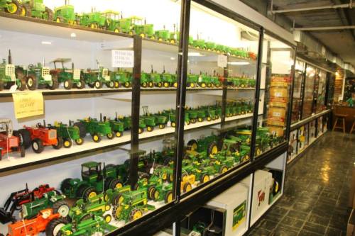 A display case filled with various green and yellow toy tractors, showcasing a collection of model farm equipment.