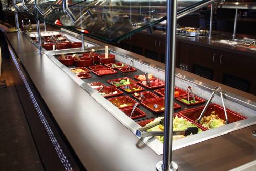 A salad bar with various toppings and ingredients in red containers, under glass covers, on a metal countertop.