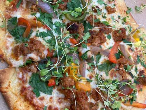 A close-up of a pizza topped with cheese, colorful peppers, herbs, and sprouts on a crispy crust.