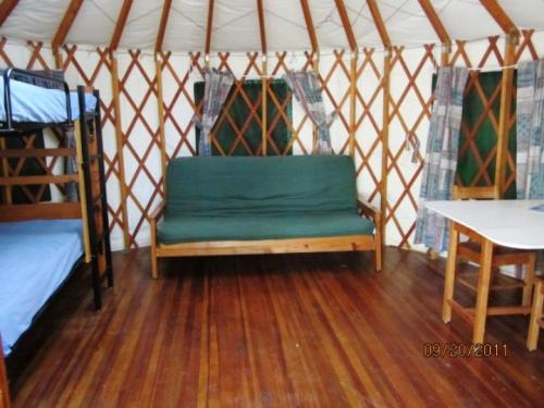 Interior of a yurt featuring bunk beds, a futon, and a table, with wooden floors and patterned curtains.