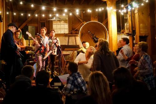 A lively band performs on stage in a rustic venue, while an engaged audience dances and enjoys the music.
