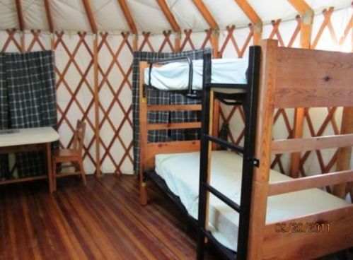 Interior of a yurt featuring two bunk beds, a wooden table, and a chair on a wooden floor.