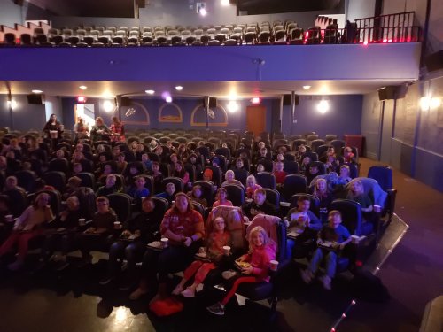 A crowded movie theater filled with children and adults sitting in seats, enjoying snacks and watching a film.