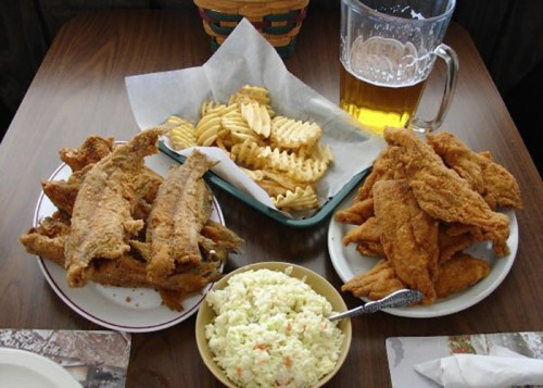 A table with fried fish, waffle fries, coleslaw, and a pitcher of beer.