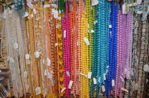 A colorful display of beaded strands in various shades, hanging in rows with tags attached.