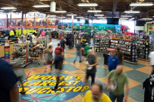 A busy interior of a large truck stop with shoppers, merchandise displays, and a colorful floor design.