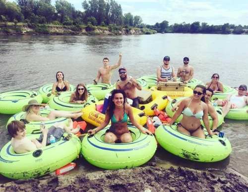 A group of people relaxing on green inner tubes in a river, enjoying a sunny day together.
