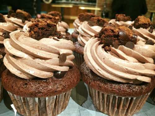 Close-up of chocolate cupcakes topped with swirls of chocolate frosting and cookie pieces.