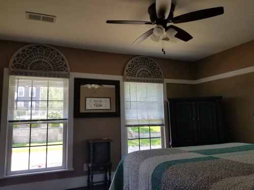 A cozy bedroom featuring a bed, decorative windows, a ceiling fan, and a dark wooden wardrobe.